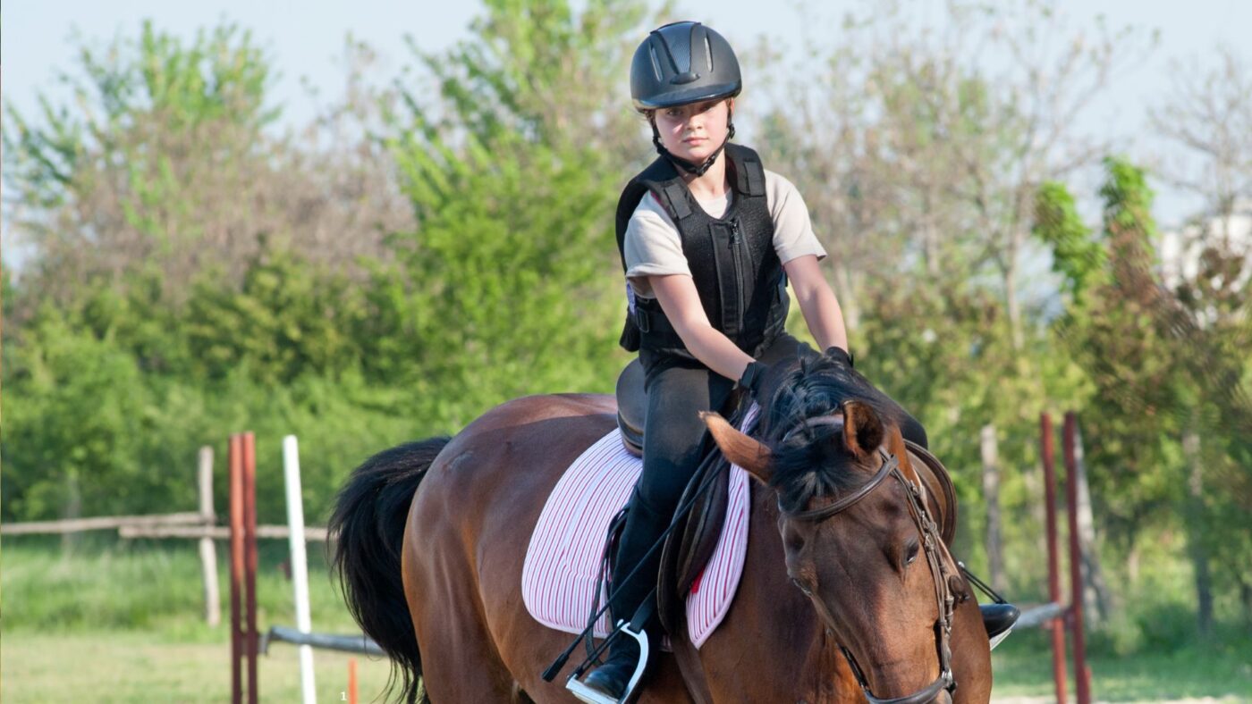 Teen child horseback riding wearing an approved riding helmet.