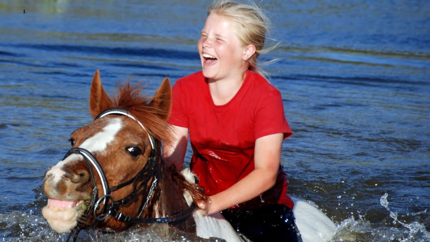 Child riding a horse while swimming in a lake on a hot day.