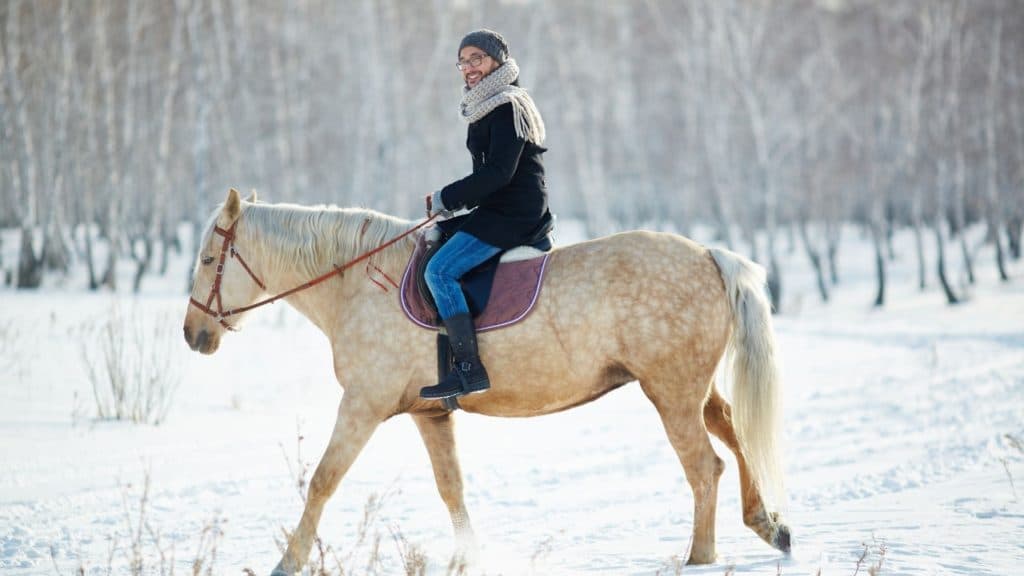 Picture of a woman riding her horse in the winter snow,