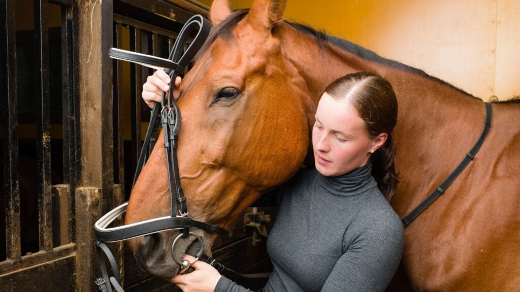 Picture of a woman putting a bridle on her horse.