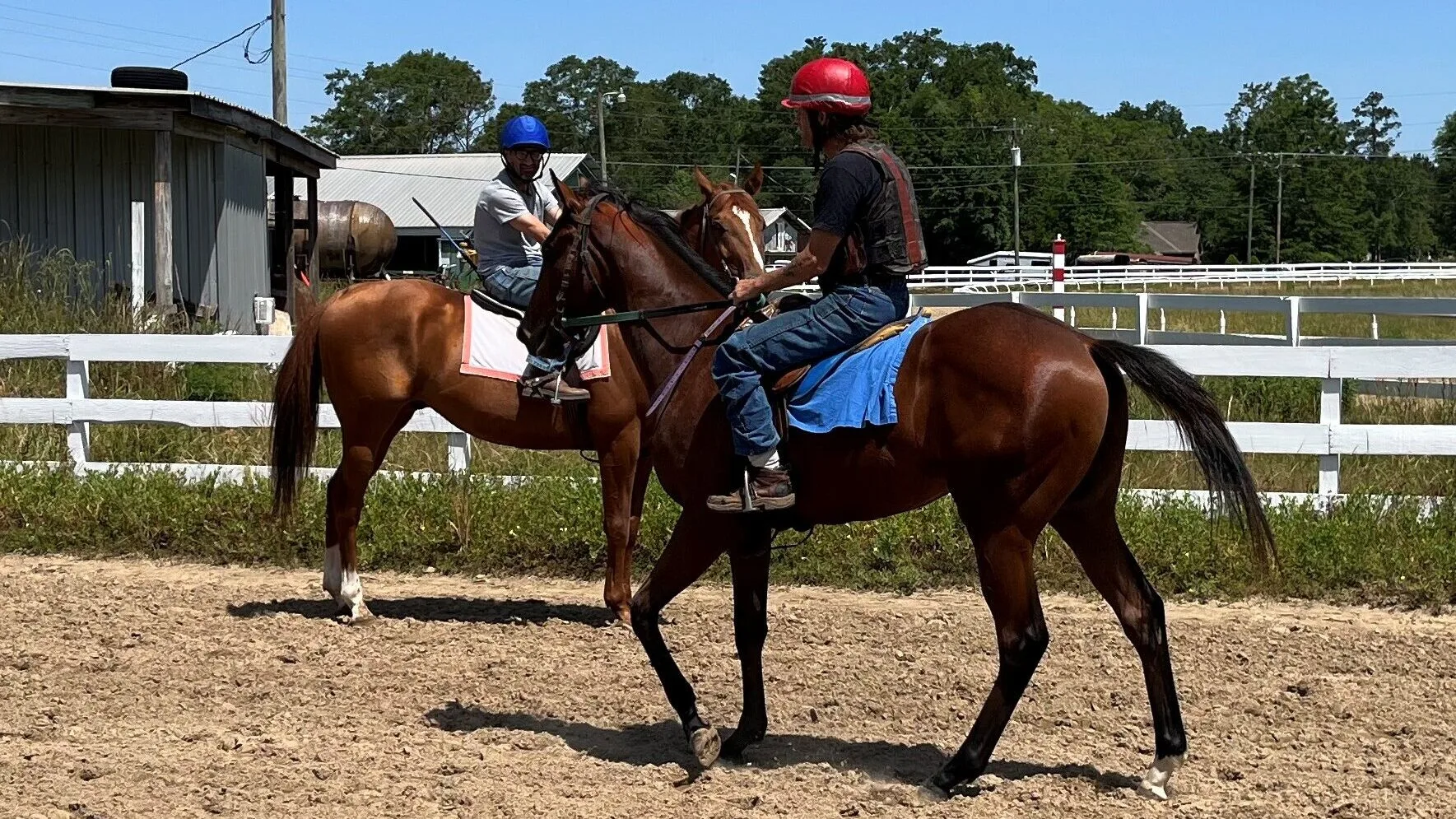 Picture of two riders on a training track, exercising horses. 