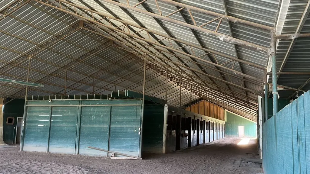 A well-ventilated horse barn with open ceilings and a high roof.