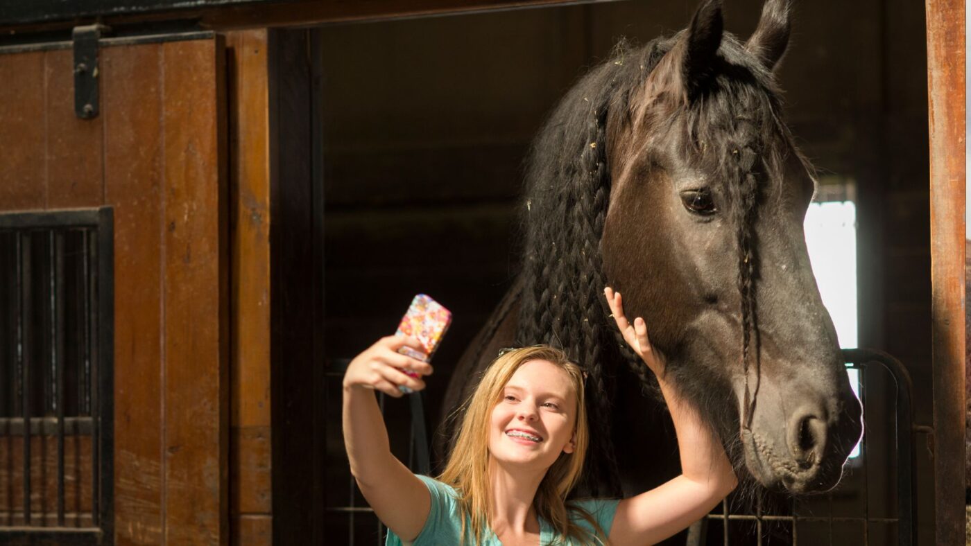 Picture of a young girl taking a selfie with a Friesian horse. 