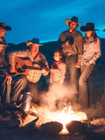 Cowboys and cowgirls wearing cowboy boos while sitting around a campfire.
