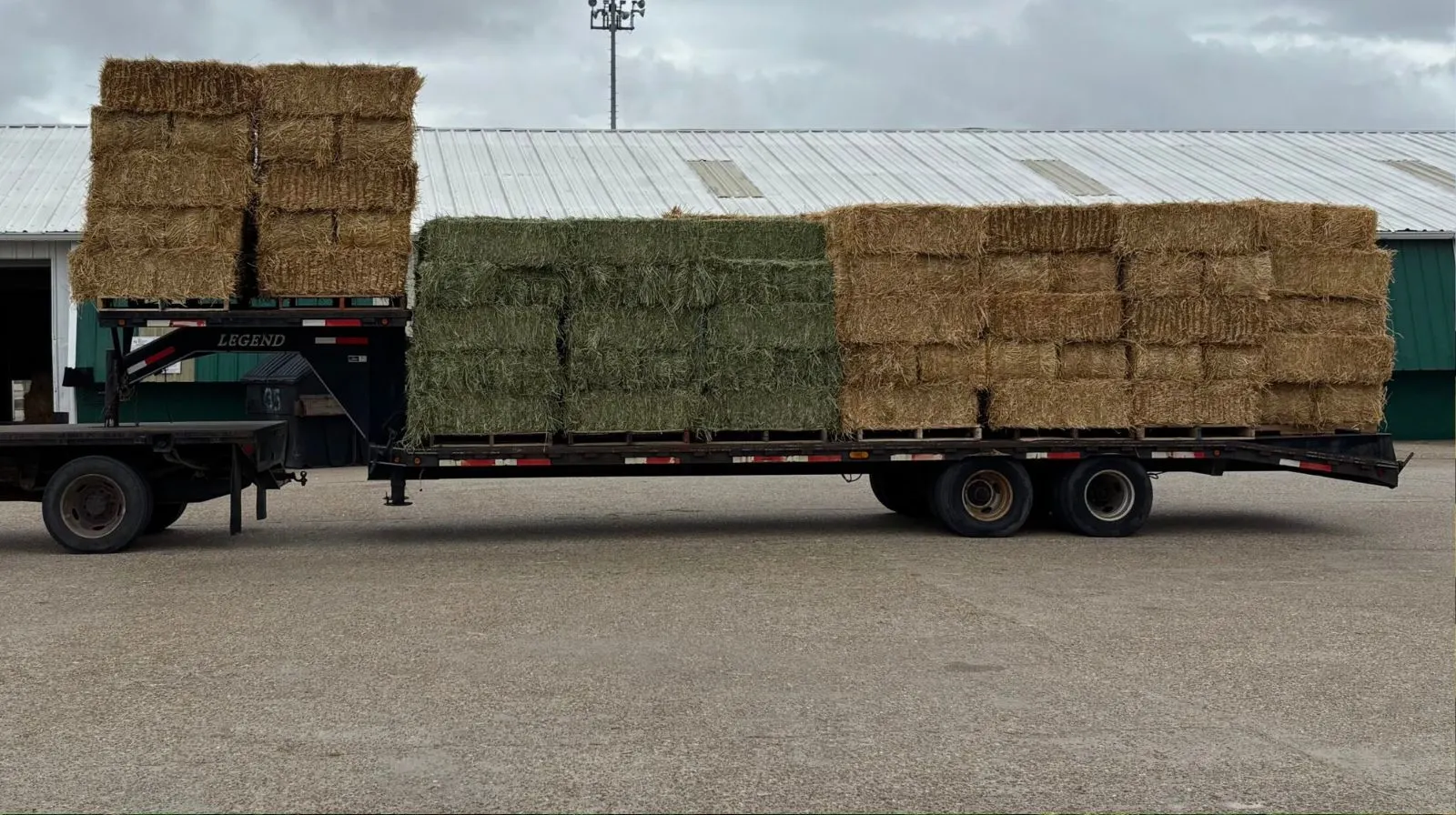 A pickup truck pulling a large trailer load of square hay bales for direct delivery from a local farmer, demonstrating a bulk savings strategy.